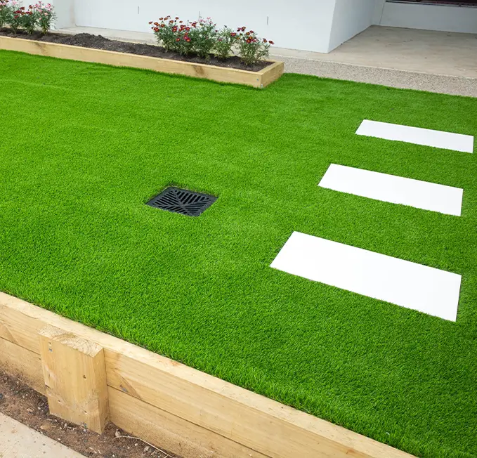 Lush artificial grass lawn featuring white paver stones and a drainage grate, ideal for landscaping and outdoor design.