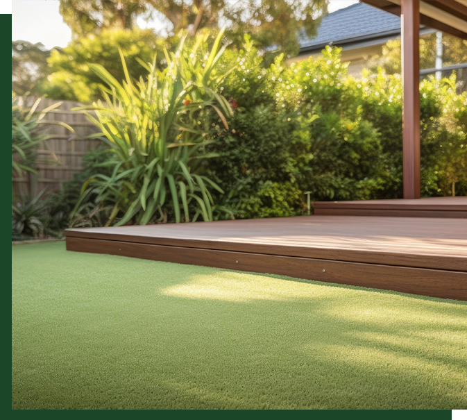 Wooden deck surrounded by artificial grass, lush greenery and plants, showcasing a natural outdoor setting with vibrant foliage.