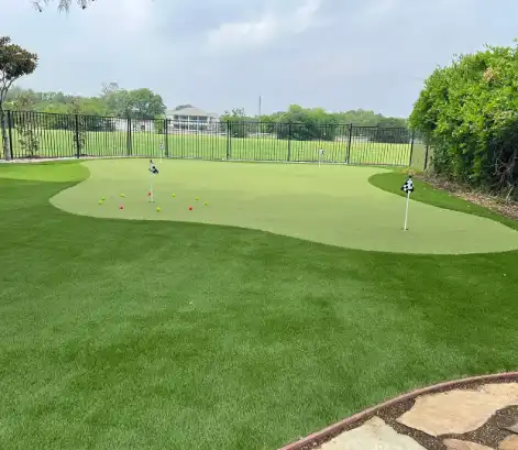 Artificial turf putting green with flags and colorful markers, designed for golf practice in a landscaped outdoor area.